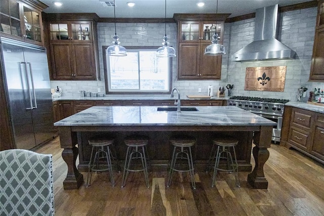 kitchen with sink, wall chimney range hood, a kitchen island with sink, and high quality appliances