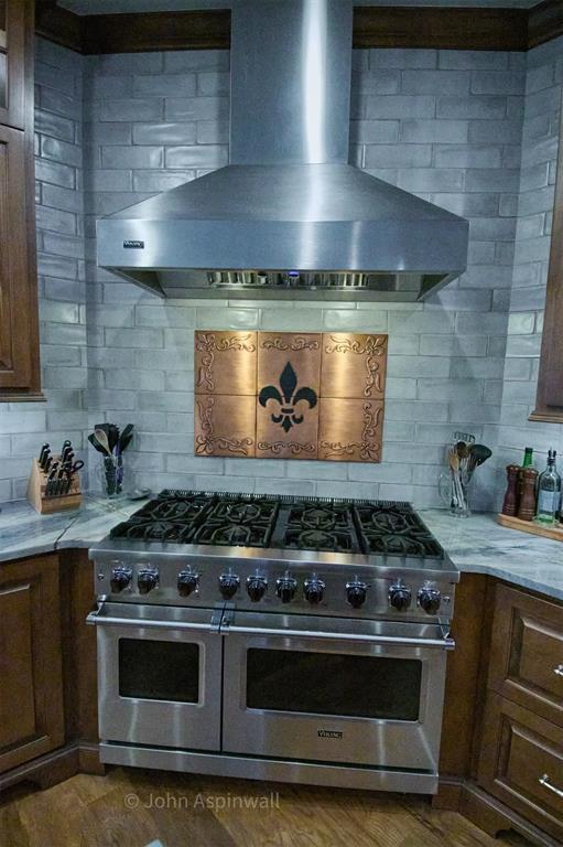 kitchen featuring wall chimney range hood, decorative backsplash, double oven range, dark hardwood / wood-style floors, and light stone counters