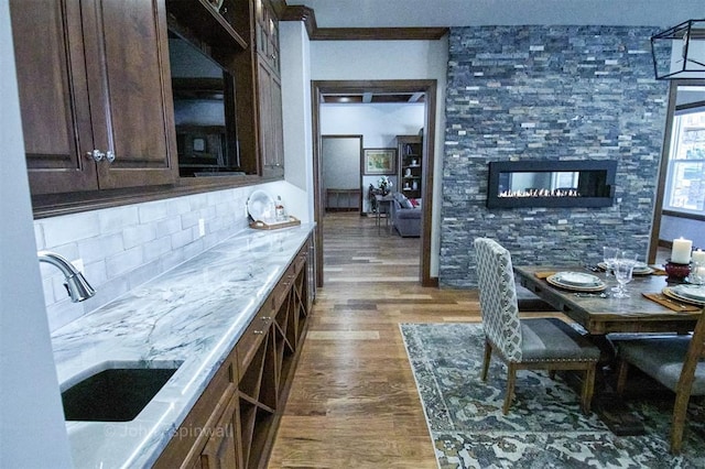 kitchen with dark brown cabinets, sink, dark wood-type flooring, light stone counters, and decorative backsplash