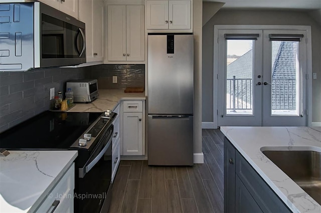 kitchen featuring light stone countertops, appliances with stainless steel finishes, tasteful backsplash, white cabinets, and french doors