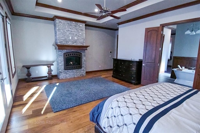 bedroom with ceiling fan, wood-type flooring, ornamental molding, and a stone fireplace