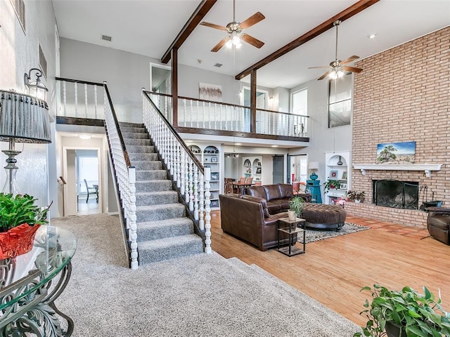 living room featuring hardwood / wood-style floors, a towering ceiling, ceiling fan, a brick fireplace, and beam ceiling