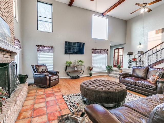 living room featuring beam ceiling, ceiling fan, a brick fireplace, and a towering ceiling