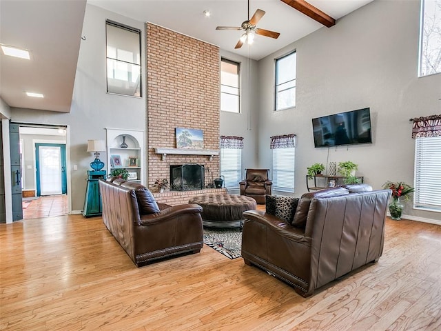 living room with ceiling fan, beam ceiling, light wood-type flooring, and a fireplace