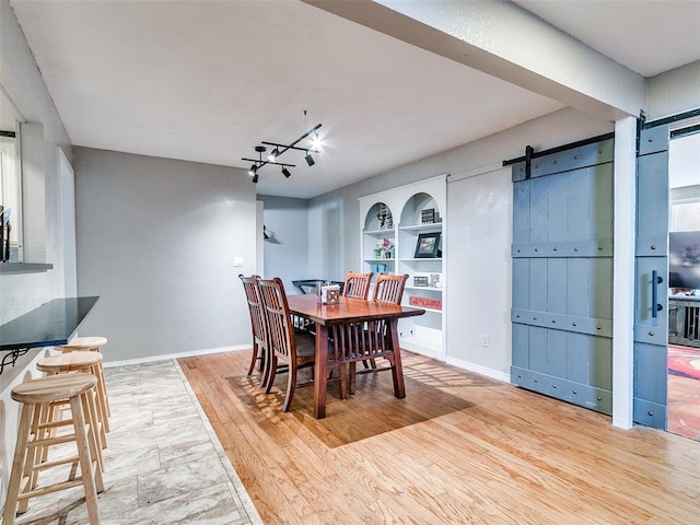 dining space with a barn door, light hardwood / wood-style flooring, and built in shelves