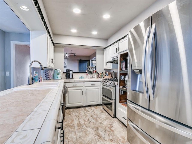 kitchen featuring tile countertops, kitchen peninsula, appliances with stainless steel finishes, white cabinets, and sink