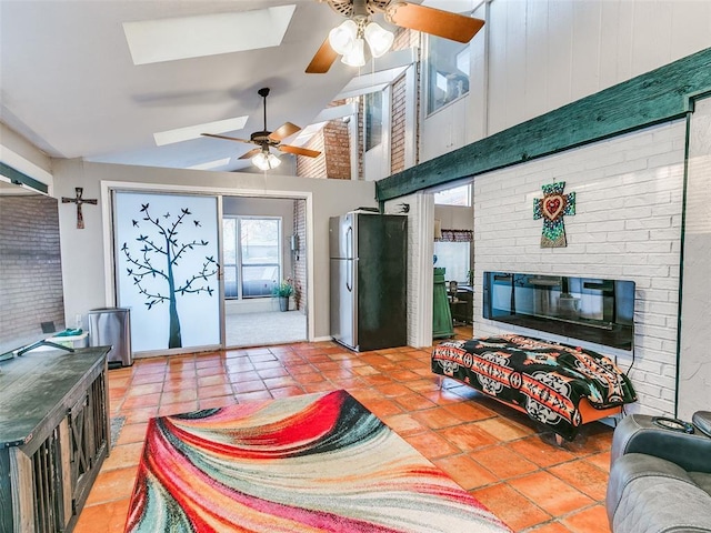 living room featuring a skylight, a brick fireplace, ceiling fan, tile patterned floors, and high vaulted ceiling