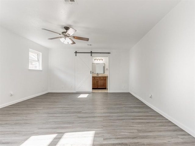 empty room with light wood-type flooring, ceiling fan, a barn door, and sink