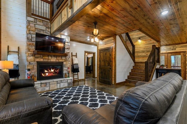 living room featuring a towering ceiling, wood ceiling, a stone fireplace, ceiling fan, and wooden walls