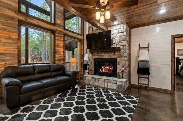 living room with a towering ceiling, ceiling fan, wood walls, wooden ceiling, and a fireplace