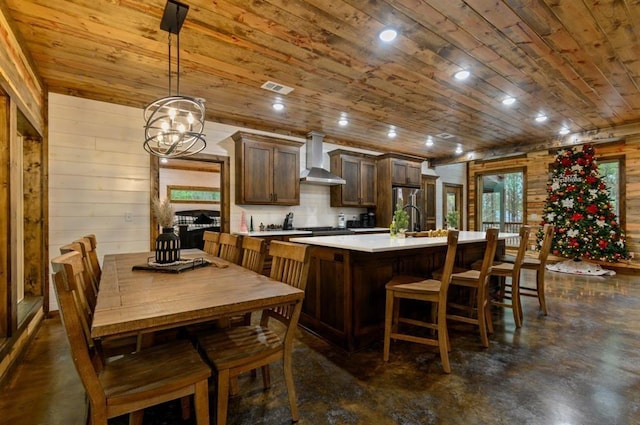 kitchen with a center island with sink, wall chimney range hood, wooden ceiling, and pendant lighting