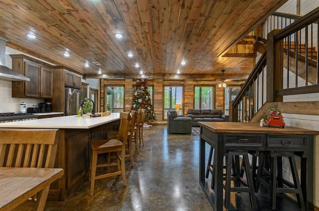 kitchen featuring wall chimney exhaust hood, high quality fridge, a kitchen bar, and wood ceiling