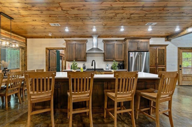 kitchen with a center island with sink, wall chimney exhaust hood, high quality fridge, and wooden ceiling