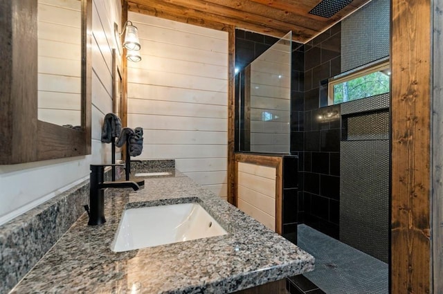 bathroom with a tile shower, vanity, and wooden walls