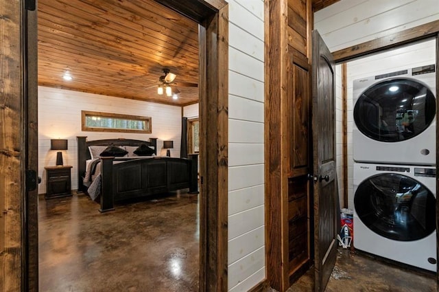 washroom featuring ceiling fan, stacked washer and dryer, wooden ceiling, and wooden walls