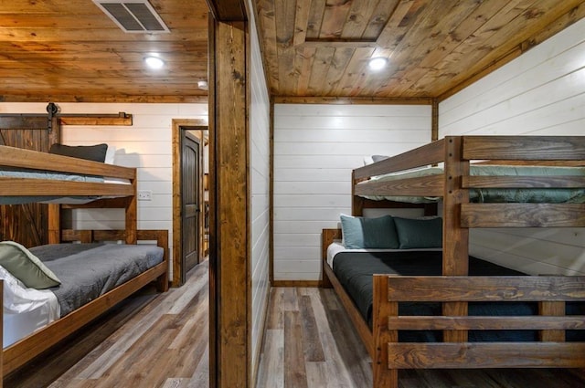 bedroom with hardwood / wood-style floors, wood walls, wooden ceiling, and a barn door