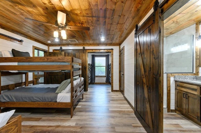 bedroom featuring wooden walls, wooden ceiling, light hardwood / wood-style floors, and a barn door