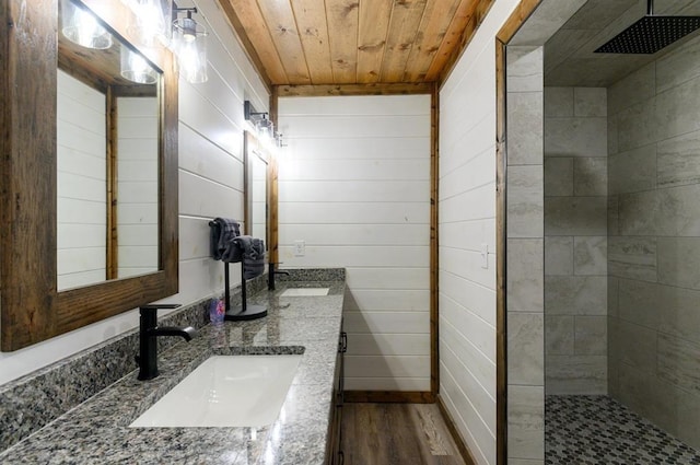 bathroom featuring wood ceiling, wood-type flooring, vanity, wooden walls, and tiled shower