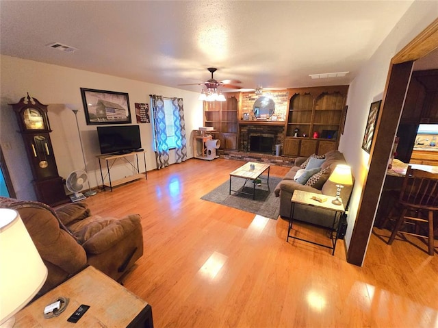 living room with built in shelves, ceiling fan, hardwood / wood-style flooring, and a fireplace