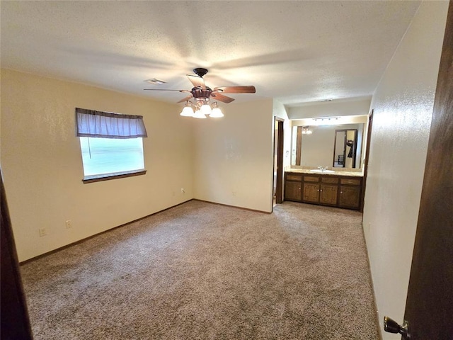 unfurnished bedroom featuring ceiling fan, connected bathroom, light carpet, and a textured ceiling