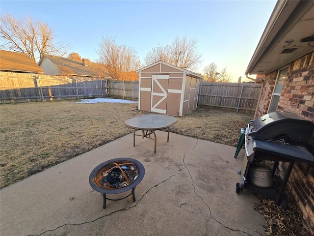 patio terrace at dusk featuring a storage unit, area for grilling, a lawn, and a fire pit