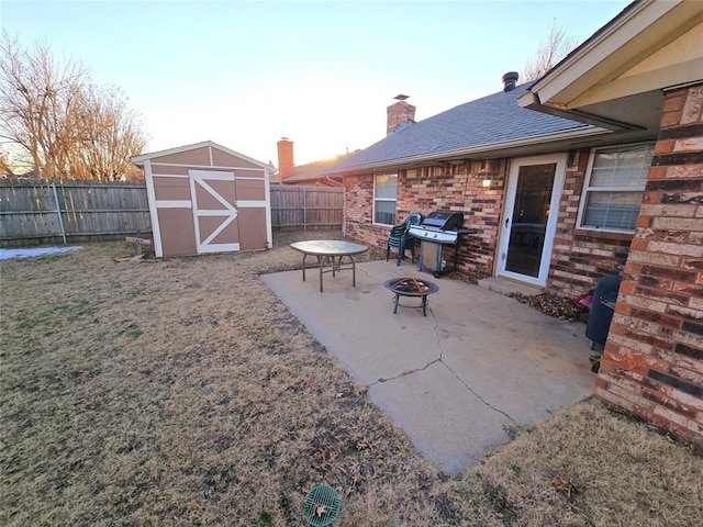 patio terrace at dusk featuring area for grilling, a storage unit, and an outdoor fire pit