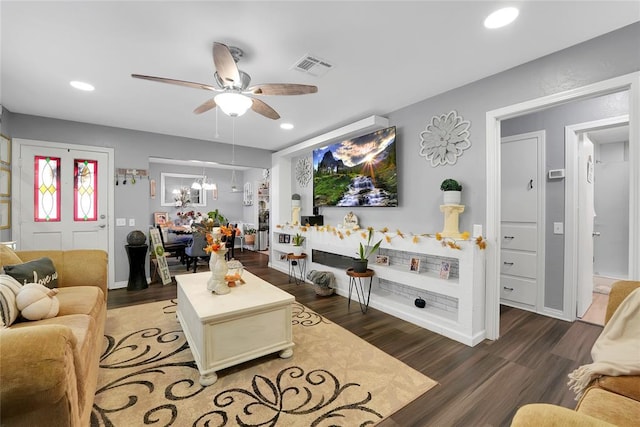 living room featuring ceiling fan with notable chandelier and dark wood-type flooring