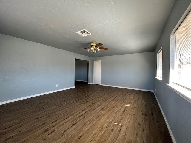 spare room with a textured ceiling, ceiling fan, dark wood-type flooring, visible vents, and baseboards