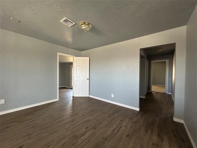 spare room featuring a textured ceiling, dark wood-type flooring, visible vents, and baseboards