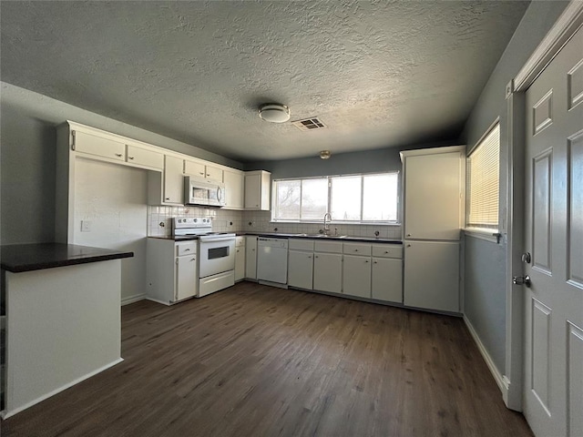 kitchen with white appliances, visible vents, dark countertops, dark wood-style flooring, and a sink