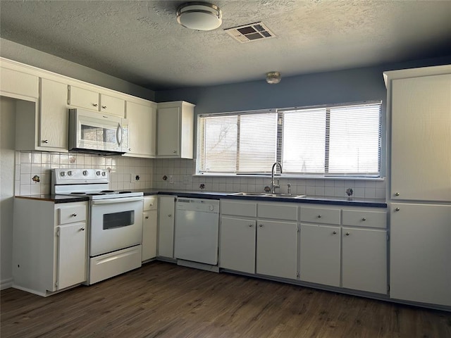 kitchen featuring white appliances, visible vents, dark countertops, dark wood-style floors, and a sink