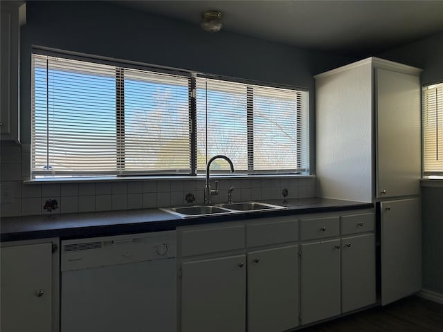 kitchen with dark countertops, backsplash, white dishwasher, and a sink