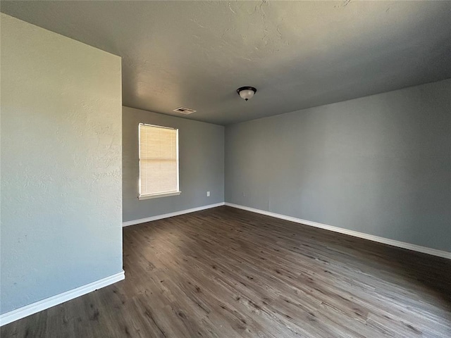 spare room with baseboards, visible vents, and dark wood-type flooring