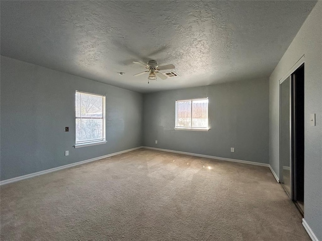 carpeted spare room featuring a ceiling fan, visible vents, a textured ceiling, and baseboards