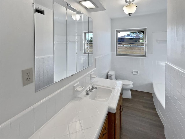 bathroom with hardwood / wood-style floors, vanity, a tub, tile walls, and toilet