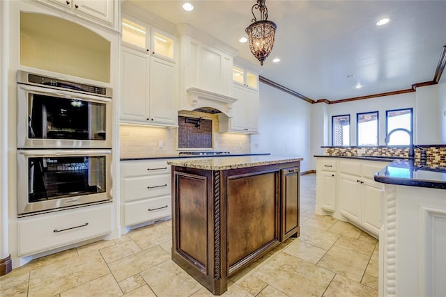 kitchen with sink, white cabinetry, hanging light fixtures, a kitchen island with sink, and double oven