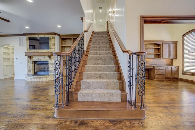 stairway featuring wood-type flooring, a fireplace, and crown molding