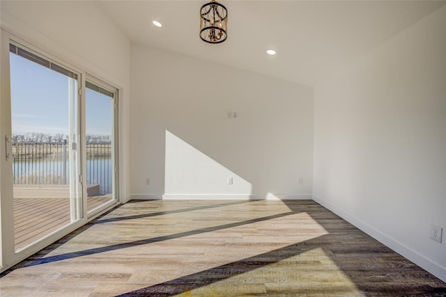 empty room with an inviting chandelier, a water view, and wood-type flooring