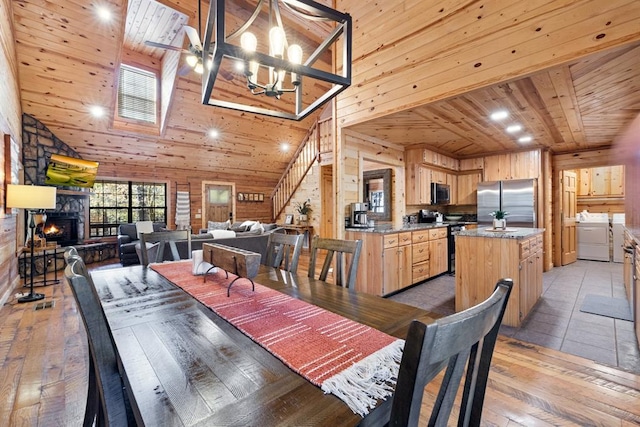 dining area with a fireplace, wood ceiling, washer and clothes dryer, high vaulted ceiling, and wood walls