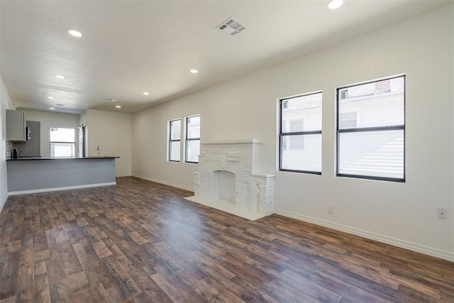 unfurnished living room featuring a wealth of natural light, dark hardwood / wood-style flooring, and a stone fireplace