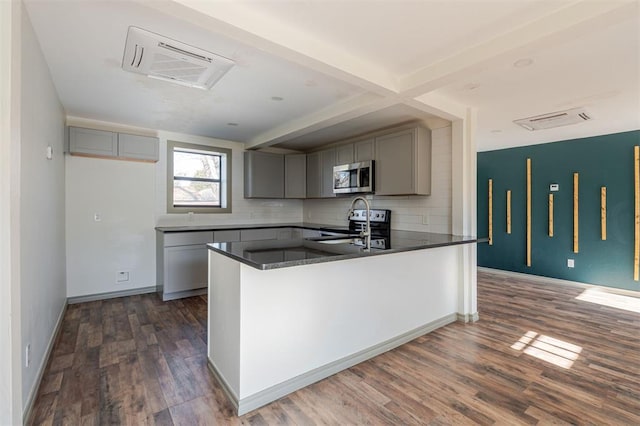 kitchen featuring dark wood-type flooring, stainless steel appliances, backsplash, gray cabinets, and kitchen peninsula