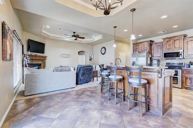 kitchen with a kitchen bar, an island with sink, stainless steel appliances, a tray ceiling, and decorative light fixtures