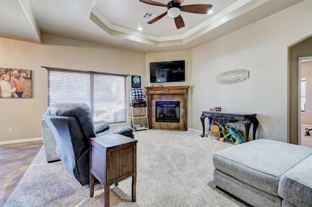 living room with ceiling fan, carpet floors, crown molding, a tray ceiling, and a tiled fireplace