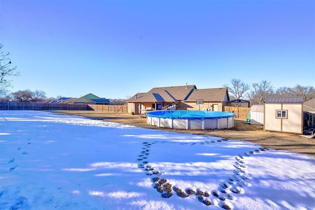 yard layered in snow featuring a covered pool and a storage unit