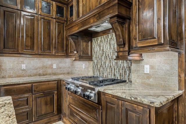 kitchen with light stone counters, dark brown cabinetry, stainless steel gas cooktop, and decorative backsplash