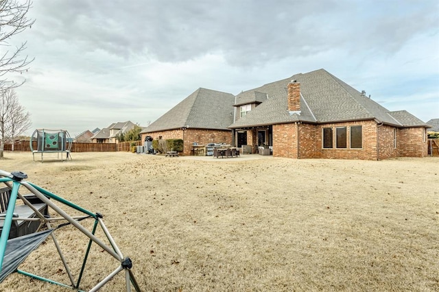 back of house featuring a trampoline, brick siding, a patio, and a fenced backyard