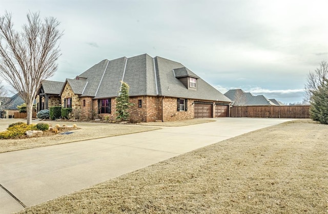 view of side of property with brick siding, driveway, an attached garage, and fence