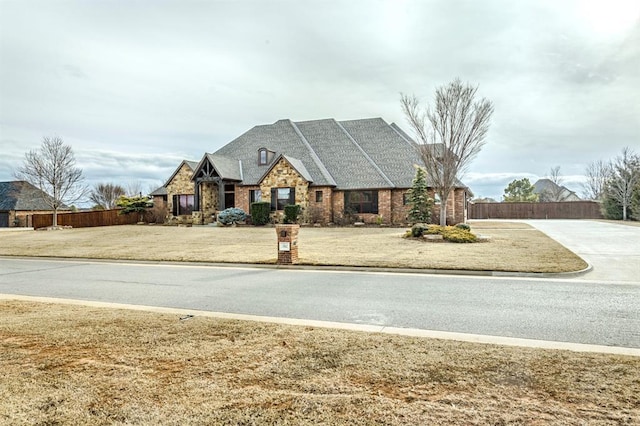 view of front of home with stone siding, a front lawn, and fence