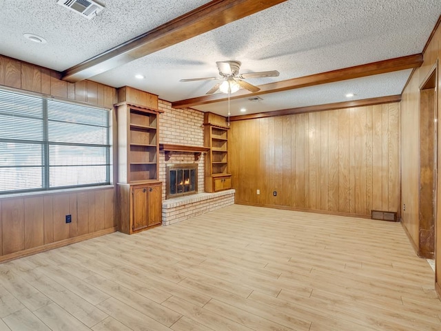 unfurnished living room featuring a textured ceiling, built in shelves, beamed ceiling, a fireplace, and wooden walls