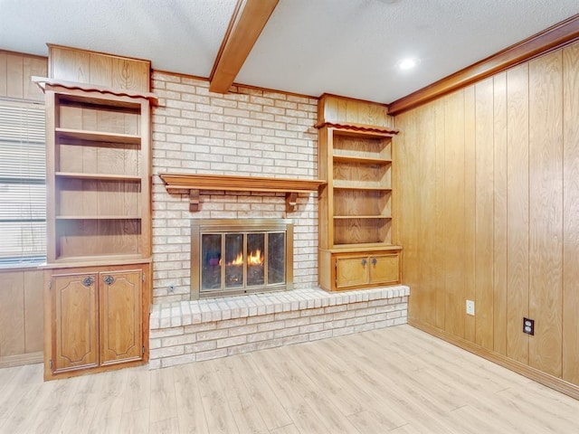 unfurnished living room featuring a brick fireplace, light hardwood / wood-style floors, beam ceiling, and wooden walls